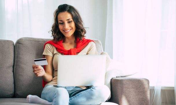 Beautiful happy young woman in casual clothes is sitting on the couch at home and doing online shopping on black friday. - Foto, Imagen