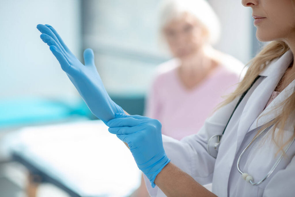 Long-haired young pretty nurse putting on protective gloves - Photo, Image