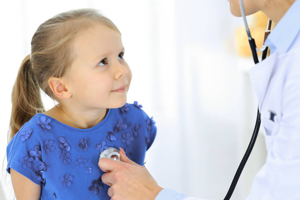 Doctor examining a little girl by stethoscope. Happy smiling child patient at usual medical inspection. Medicine and healthcare concepts - Фото, зображення
