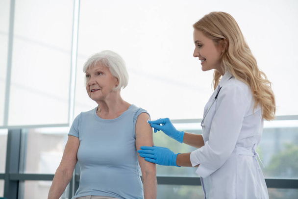 Pretty young nurse making vaccination to an elderly woman - Photo, Image