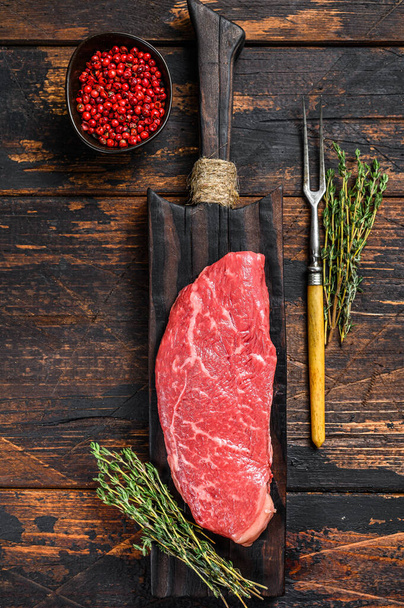 Nyers csíkos steak egy vágódeszkán, márványos marhahús. Sötét Fa háttér. Felülnézet. - Fotó, kép