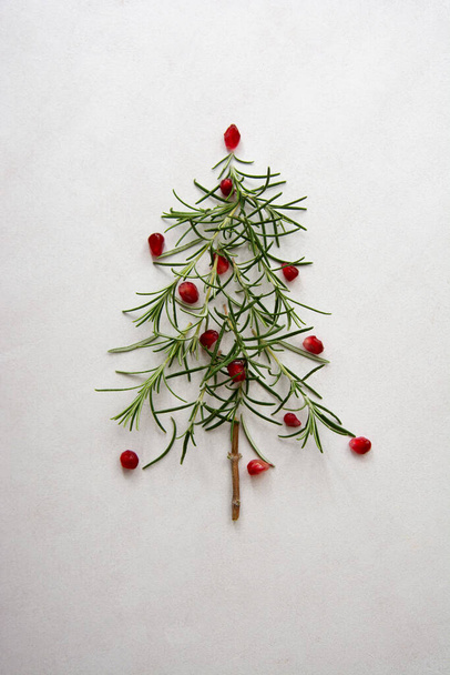 Kerstboom gemaakt van rozemarijn en granaatappel op witte achtergrond. Abstract voedsel. - Foto, afbeelding