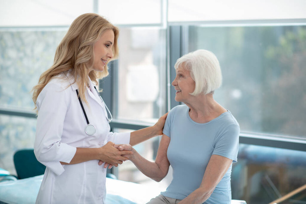 Long-haired cute smiling nurse talking to an elderly patient - Photo, Image