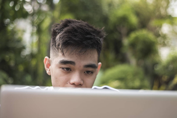 Ένας νεαρός Φιλιππινέζος είναι απασχολημένος με το λάπτοπ μελετώντας για το διαδικτυακό του μάθημα. Πυροβολήθηκε σε κήπο έξω από το σπίτι. - Φωτογραφία, εικόνα