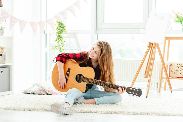 Pretty girl playing guitar sitting on floor - Фото, изображение