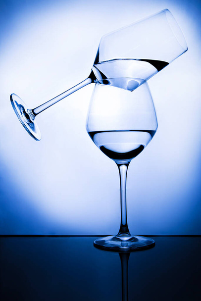 Dvě průhledné sklenice vína s vodou vyvažující na modrém světlém pozadí. Geometrický, vyvážený a abstraktní koncept - Fotografie, Obrázek