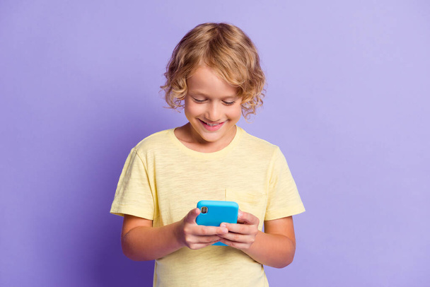 Photo of positive little boy chatting on cellphone wear yellow t-shirt isolated over violet color background - Foto, Imagem