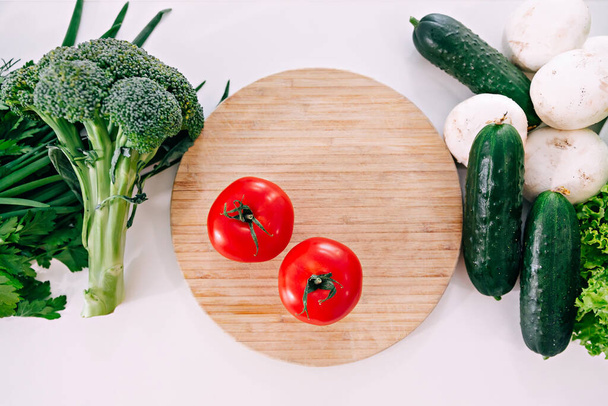 Verscheidenheid van verse groenten geplaatst op houten snijplank met mes op tafel. - Foto, afbeelding