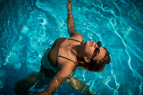 Μόδα πορτρέτο χαριτωμένο χαριτωμένο κορίτσι σε κομψά γυαλιά ηλίου ποζάρουν στην πισίνα κατά τη διάρκεια των διακοπών σε πολυτελές θέρετρο. Χαρούμενος συν μέγεθος έφηβος κορίτσι απολαμβάνει. χαρούμενη, θετική συγκίνηση, καλοκαιρινό στυλ. - Φωτογραφία, εικόνα