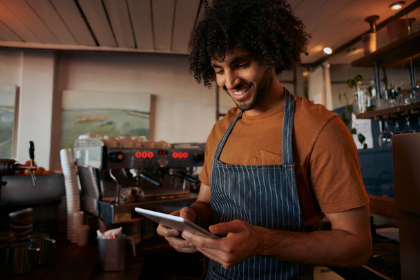 Young man in apron using digital tablet at his cafe - Foto, immagini