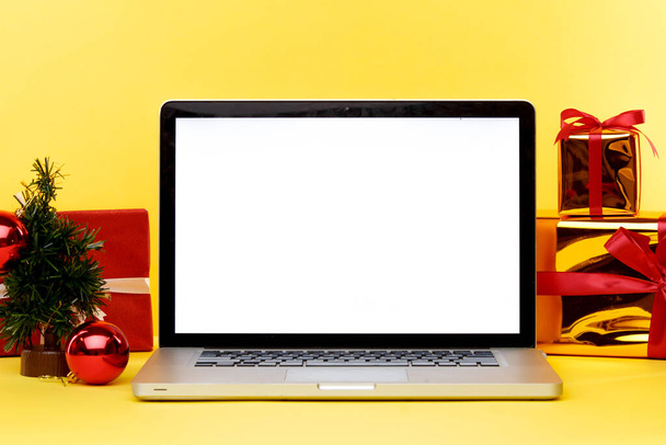 Online kerst shopping concept op de laptop display. Wit scherm op de computer en geschenken met papieren tassen in de buurt. - Foto, afbeelding