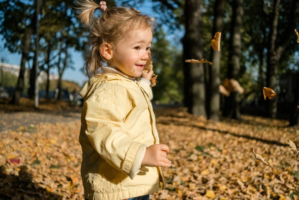 Kaukasisches Mädchen wirft im Herbst Blätter in den Park. - Foto, Bild