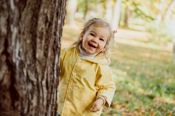 Caucasian child girl playing hide and seek in the park in autumn. - Foto, Bild