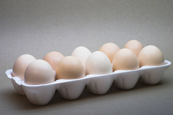 Chicken eggs close-up in a white polymer tray on a cardboard background. - Fotó, kép