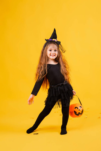 Klein meisje met lang rood haar lacht in een Halloween heksenkostuum. Halloween voor kinderen, ruimte voor tekst - Foto, afbeelding