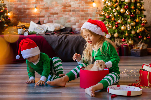 Kaksi pientä lasta pyjamassa ja jouluhatuissa purkaa joululahjat huoneessa - Valokuva, kuva