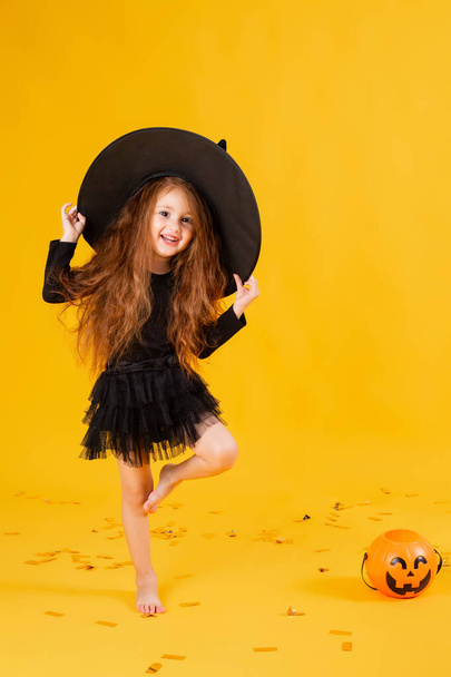 little girl with long red hair  in a Halloween witch costume on a yellow background. Halloween for children, space for text - Foto, Bild