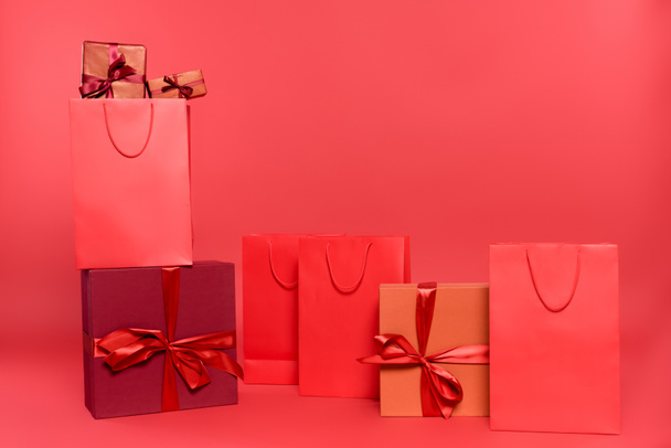 Κουτιά δώρων με φιόγκους και τσάντες αγορών σε κόκκινο φόντο - Φωτογραφία, εικόνα