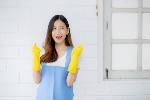 Portret młoda Azjatka jest gospodyni w gumowych rękawiczkach i fartuchu do ochrony w domu, mundur pokojówki, sprzątanie i pranie, dziewczyna stoi pracownik pozytywny, jedna osoba, koncepcja stylu życia. - Zdjęcie, obraz