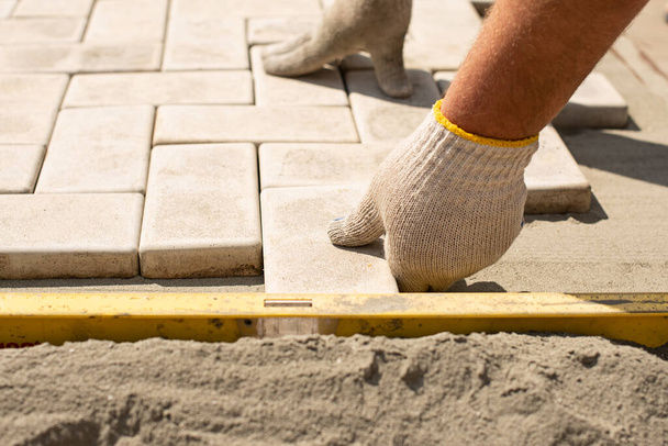 The master lays paving stones in layers. Garden brick pathway paving by professional paver worker. Laying gray concrete paving slabs in house courtyard on sand foundation base. - Photo, Image
