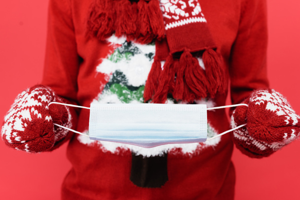 Cropped view of man in mittens holding medical mask on blurred background isolated on red  - Fotografie, Obrázek
