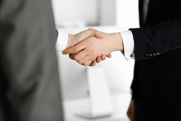 Unknown businessman shaking hands with his colleague or partner while standing straight in modern office, close-up. Business people group at meeting - Photo, Image