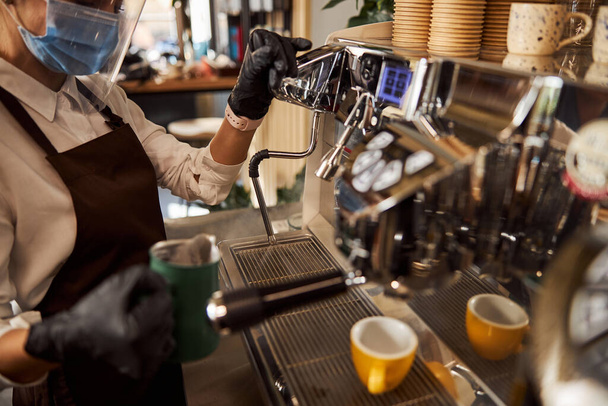 Mujer en máscara médica haciendo café en la cafetería - Foto, imagen