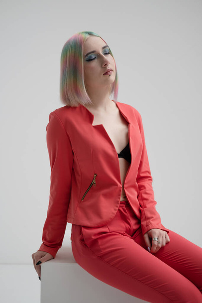 Portrait of a young beautiful informal blonde girl with dyed hair. Red jacket suit on the naked body. Studio photoshoot on a white background. - Фото, изображение