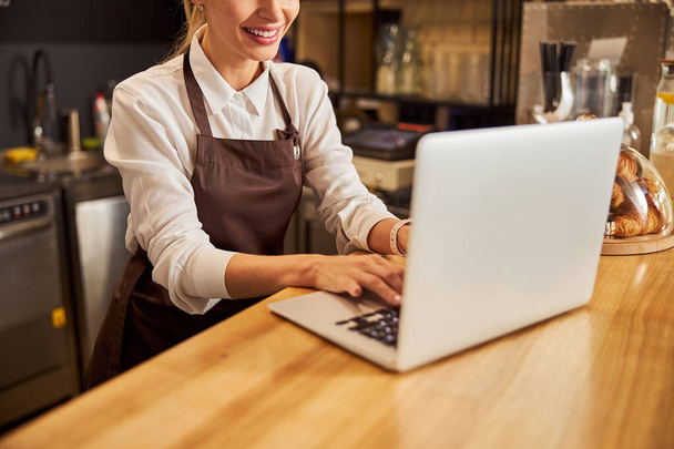 Saleswoman in uniform typing report on the computer in coffee bar - Foto, Bild