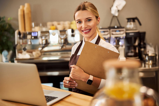 Jonge vrolijke ondernemer houdt klembord in de hand in het cafe - Foto, afbeelding