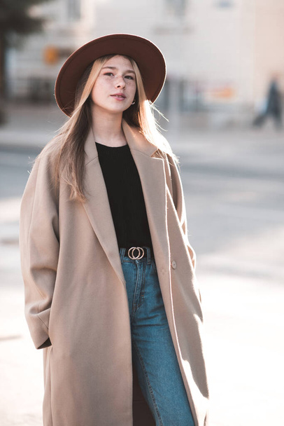 14-15 éves tinédzser lány alkalmi kalapot és télikabátot visel a városi utcában. Nézem a kamerát. Tinédzserkor.  - Fotó, kép