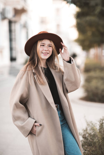 Усміхнена дівчина-підліток 14-15 років одягнена в капелюх і зимове пальто, що йде на вулиці міста крупним планом. Дивлячись на камеру. Підлітковість
.  - Фото, зображення