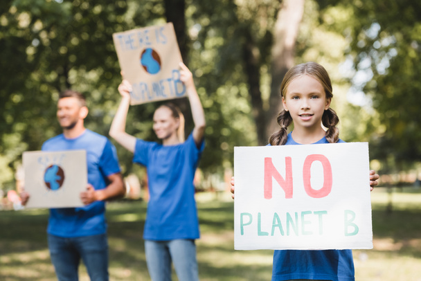niña sosteniendo cartel sin inscripción planeta b cerca de los padres con pancartas sobre fondo borroso, concepto de ecología - Foto, Imagen