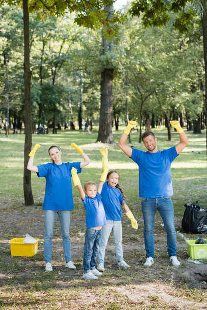 familia emocionada mostrando gesto de éxito cerca de contenedores de basura con residuos de plástico, concepto de ecología - Foto, Imagen