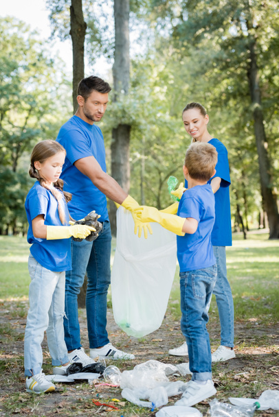 familia de voluntarios en guantes de goma recogiendo basura en bolsa de plástico reciclado en el bosque, concepto de ecología - Foto, Imagen
