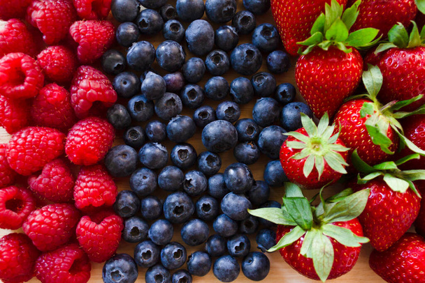 Čerstvé jahody, borůvky a maliny.Barevné čerstvé lesní ovoce na dřevěné desce pozadí. - Fotografie, Obrázek