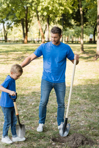father and son digging ground in forest with shovels, ecology concept - Фото, изображение