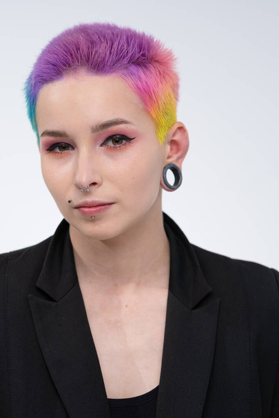 A young beautiful girl with short colored hair. Spread bright coloring and creative make-up. Piercing on the face. A black jacket. - Foto, afbeelding