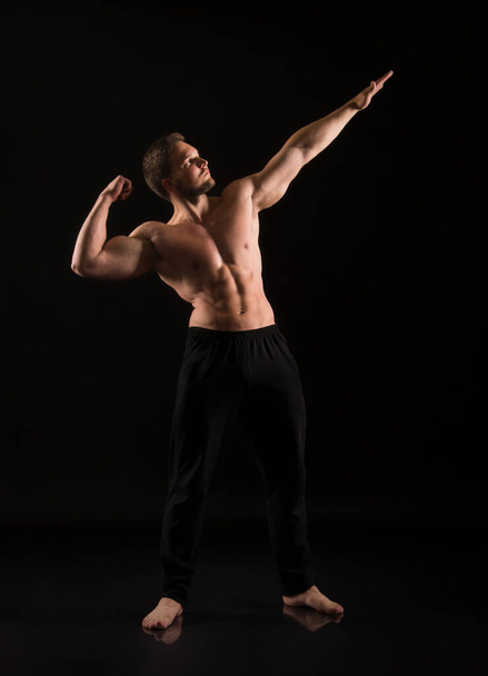 Strong athletic man showes naked muscular body. Studio shooting on a dark background. - 写真・画像