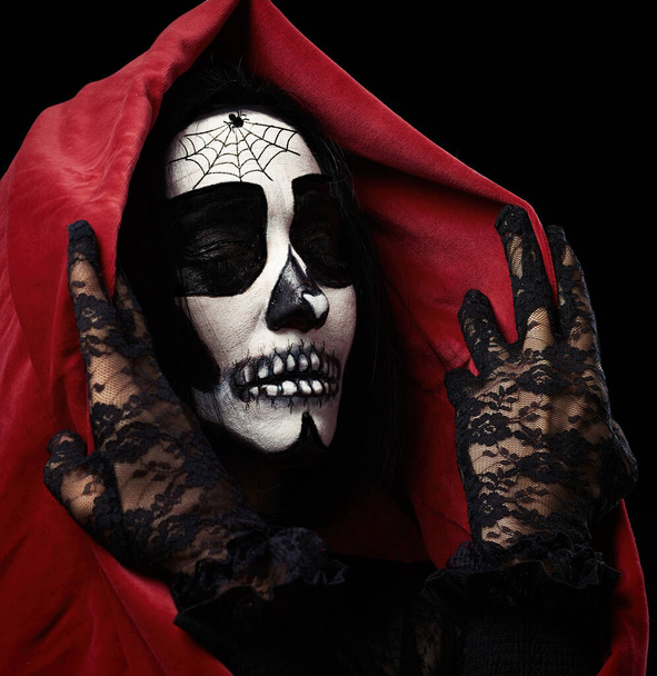 Frau mit geschminktem Skelett steht auf schwarzem Hintergrund in rotem Umhang mit Kapuze, fiktives Bild für Halloween - Foto, Bild