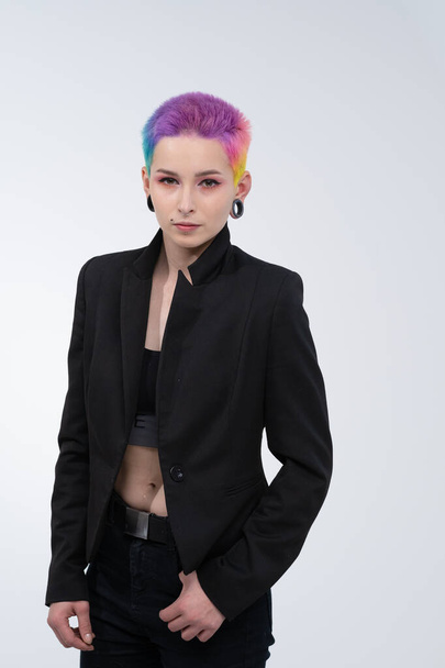 A young beautiful girl with short colored hair. Spread bright coloring and creative make-up. Piercing on the face. A black jacket. - Photo, Image