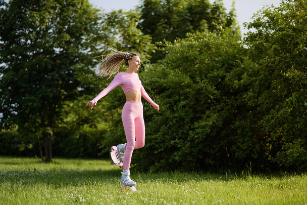 A young slender beautiful woman with dreadlocks in sportswear trains in the park outdoors. Kangoo jumps training. - Fotografie, Obrázek