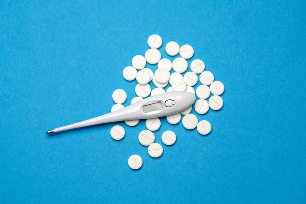 group of white pills or tablets and electronic digital thermometer on blue background - Φωτογραφία, εικόνα