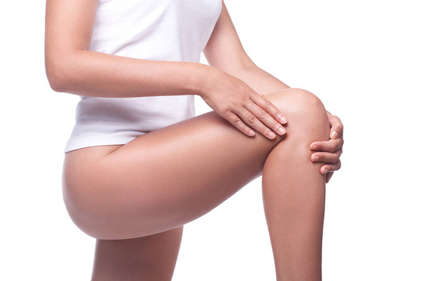 Женщина, страдающая от боли в суставах, спортивной травмы колена, молодая женщина в нижнем белье, забота о здоровье и уходе за телом, на белом фоне - Фото, изображение