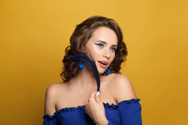 Mavi göz makyajlı, sarı arka planda mavi bluz giyen mükemmel bir genç kadın. - Fotoğraf, Görsel