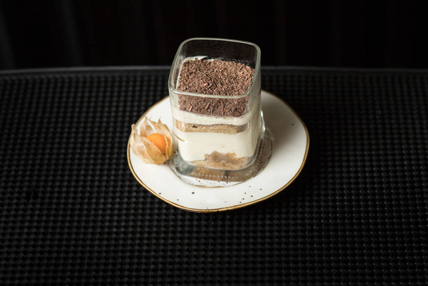 Odizolowano tradycyjny włoski deser w szklance. Tiramisu na białym talerzu z kwiatem projektu - Zdjęcie, obraz