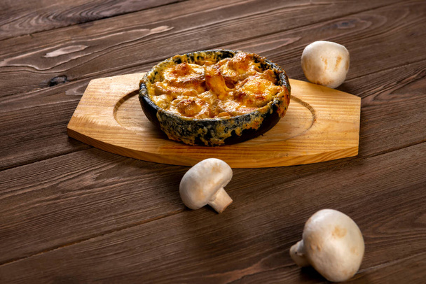 Julienne in a pot and mushrooms  on a wooden  table. Mushrooms baked with cheese crust in pan  .top view - Foto, Imagen