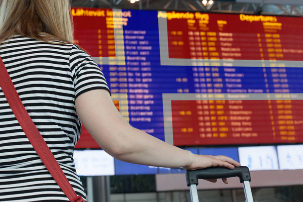 Kobieta patrzy na tablicę wyników na lotnisku. Wybierz kraj Norwegia do podróży lub migracji. - Zdjęcie, obraz