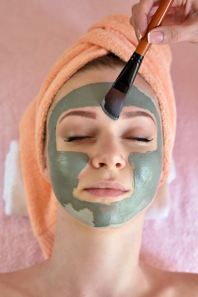 Mascarilla de descamación facial, tratamiento de belleza spa, cuidado de la piel. Mujer recibiendo cuidado facial por esteticista en el salón de spa, vista lateral, primer plano - Foto, imagen