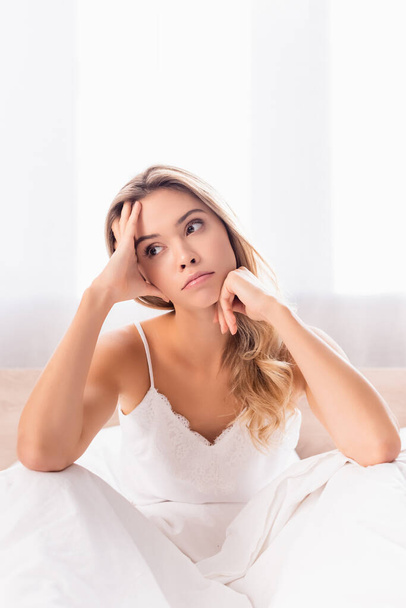 Pensive woman in pajamas sitting on bed at morning  - Photo, image